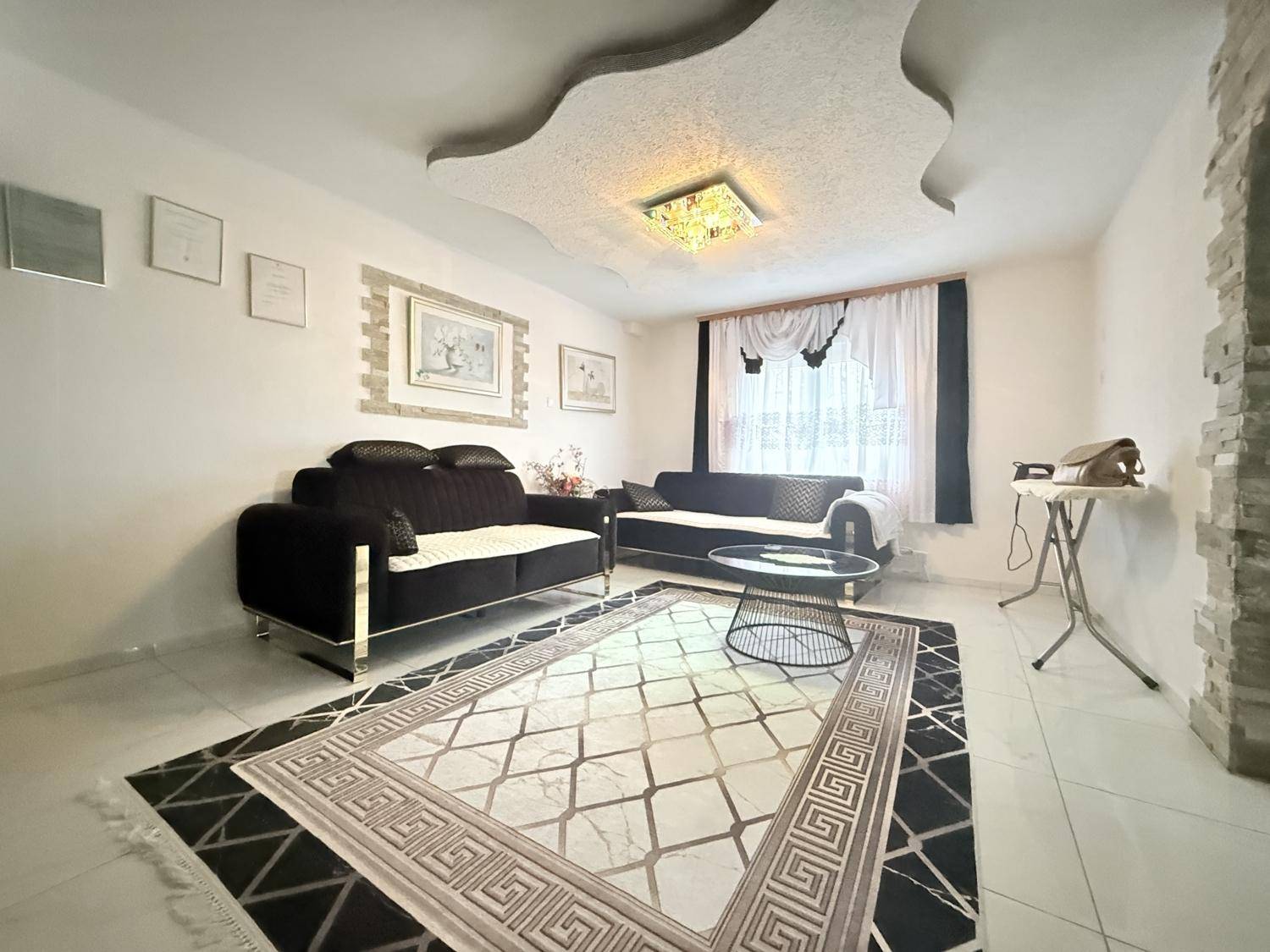 Gemütliches Wohnzimmer mit dunklen Sofas, Teppich und dekorativer Deckenbeleuchtung.