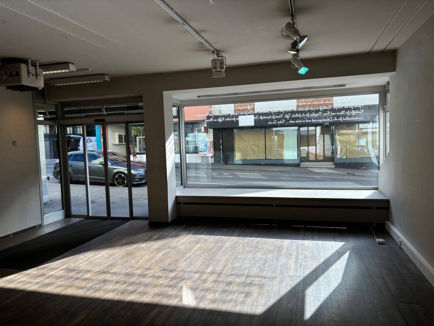 Eingangsbereich eines Ladenlokals mit großen Schaufenstern und automatischen Glastüren zur Straße.