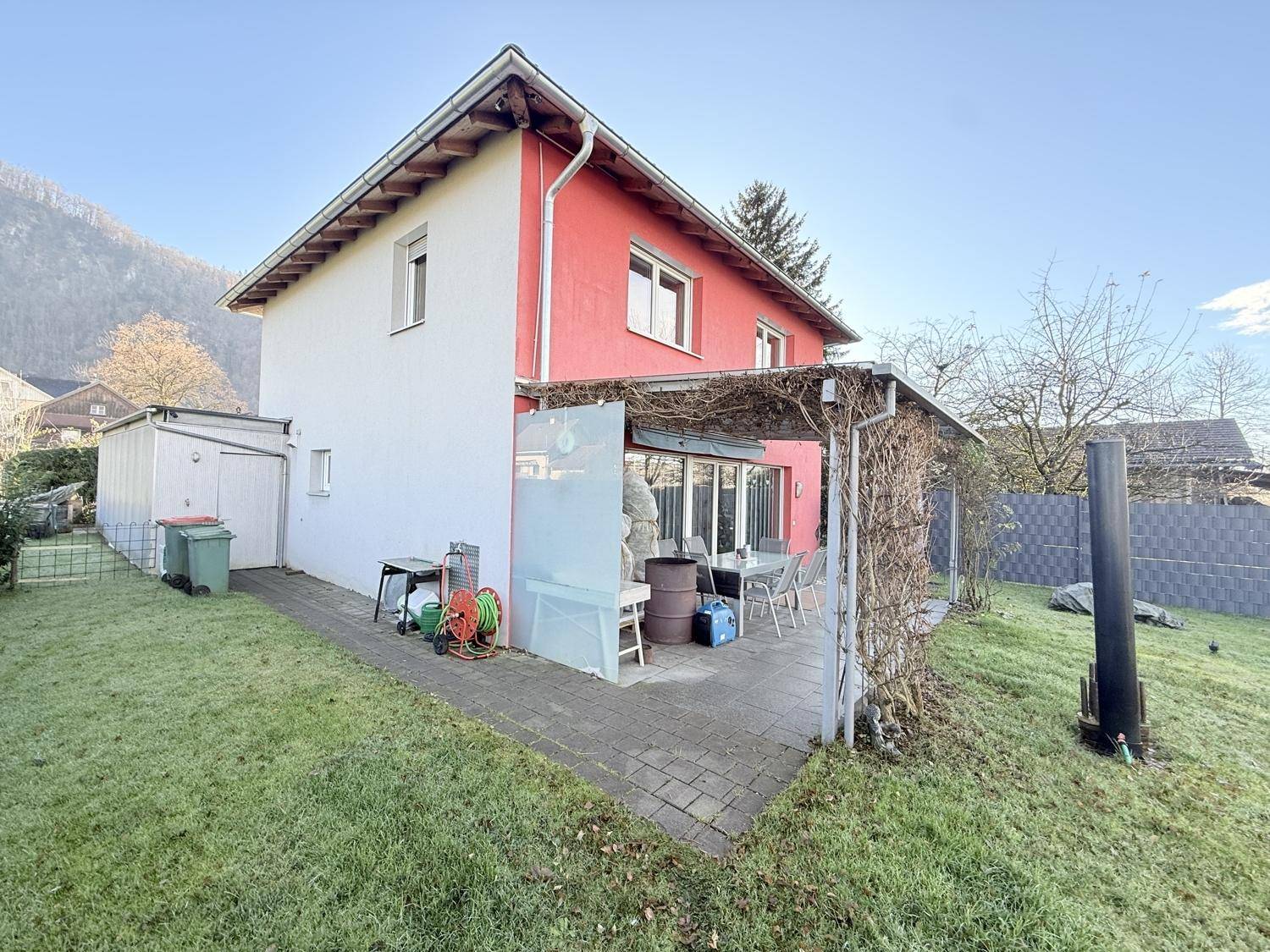Hausrückseite mit überdachter Terrasse, Garten und Geräteschuppen.