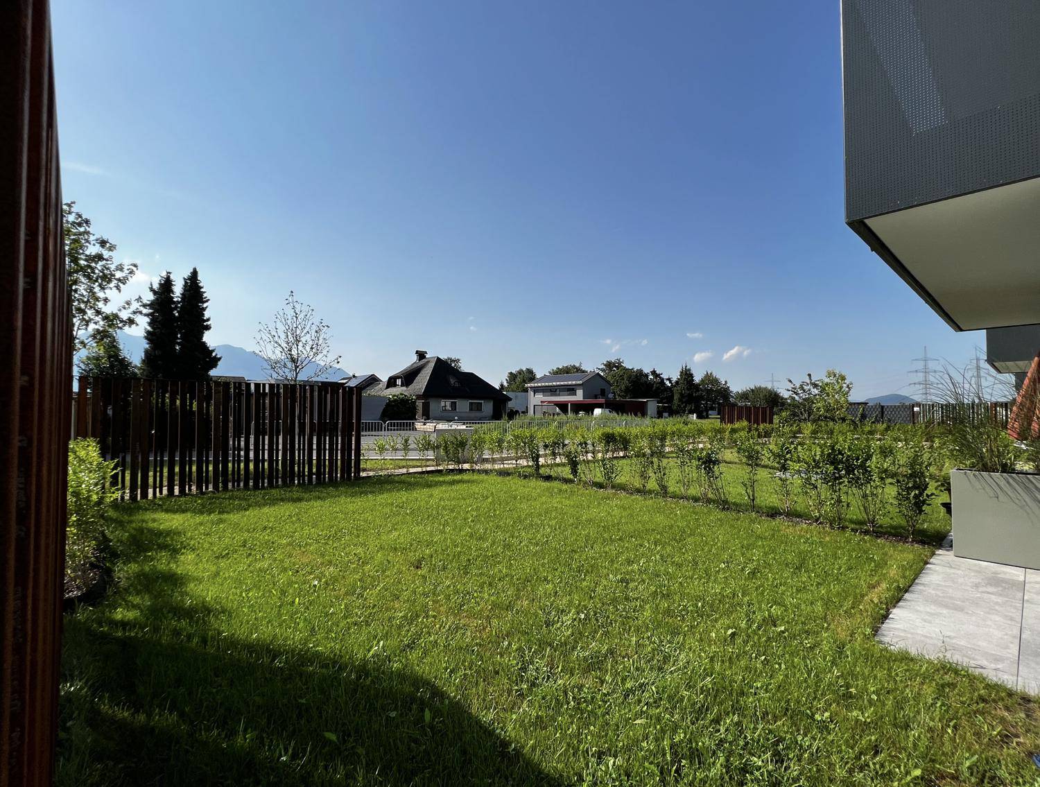 Gepflegte Rasenfläche neben dem Gebäude mit Hecke und Blick auf die Umgebung.
