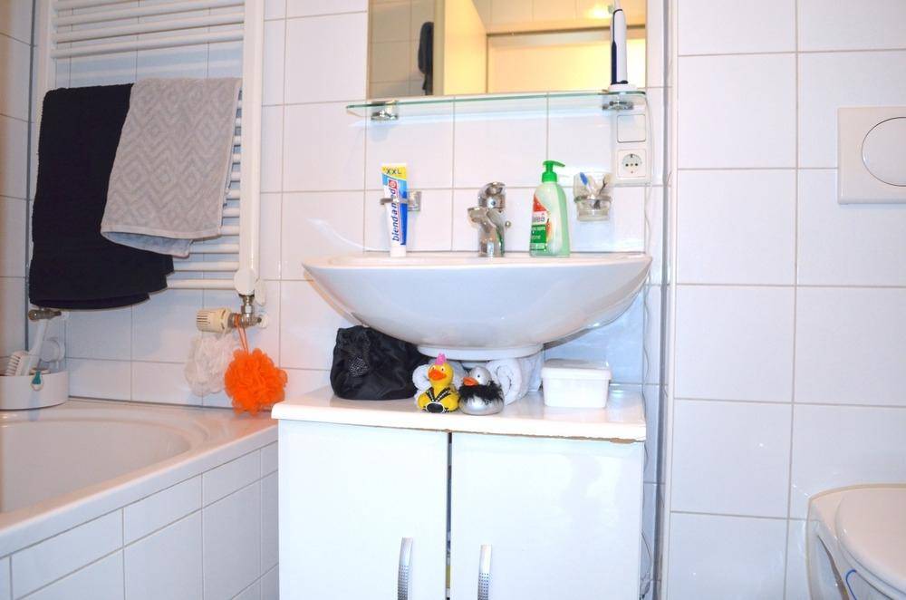 Helles Badezimmer mit weißen Fliesen, Badewanne, Waschbecken und beheiztem Handtuchhalter.