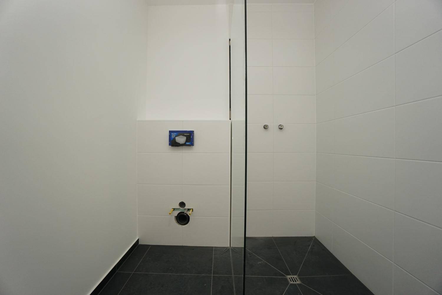 Modernes Badezimmer mit ebenerdiger Dusche, weißen Wandfliesen und dunklem Boden.