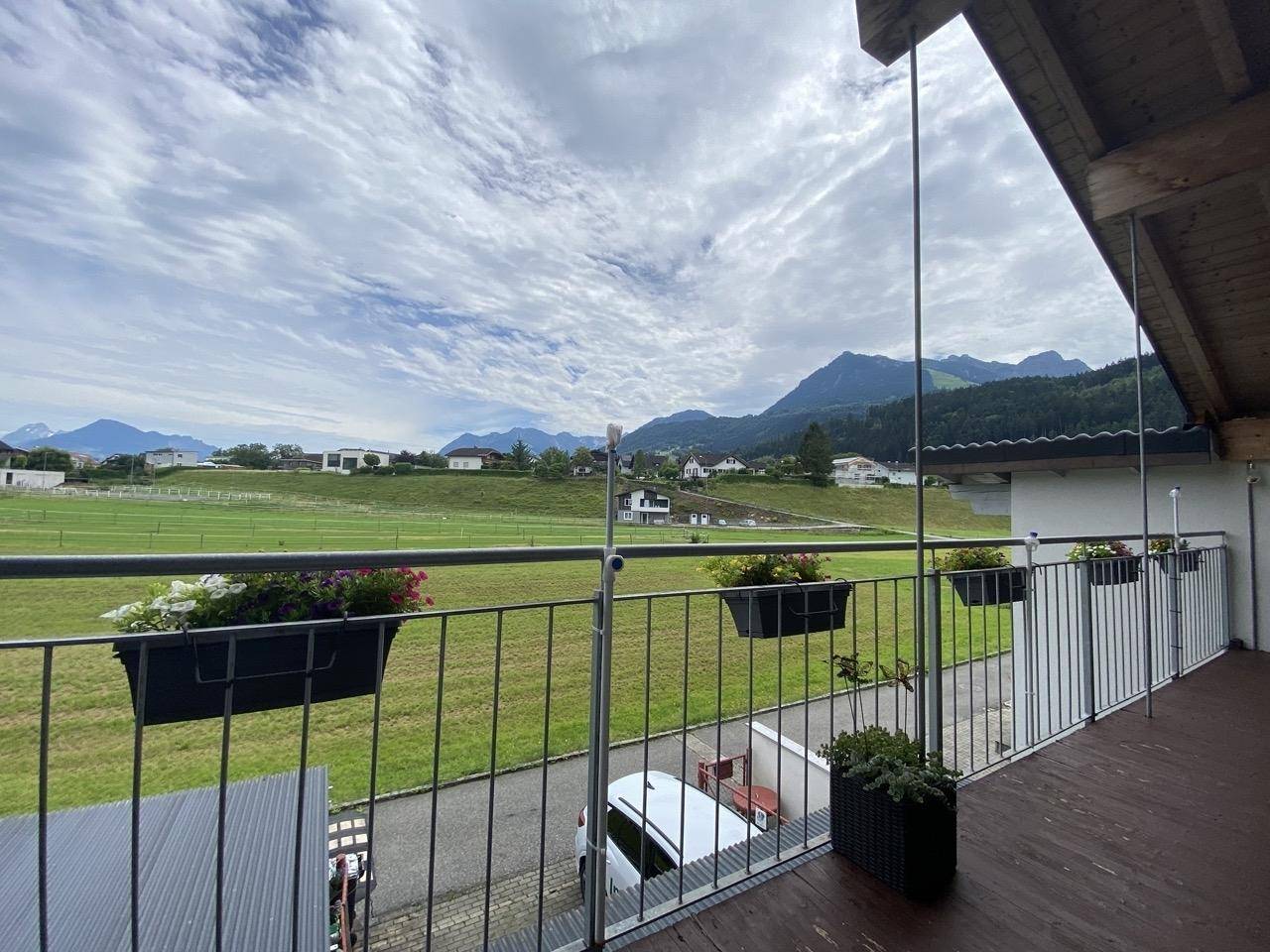 Balkon mit weitem Blick über grüne Felder und die umliegenden Berge.