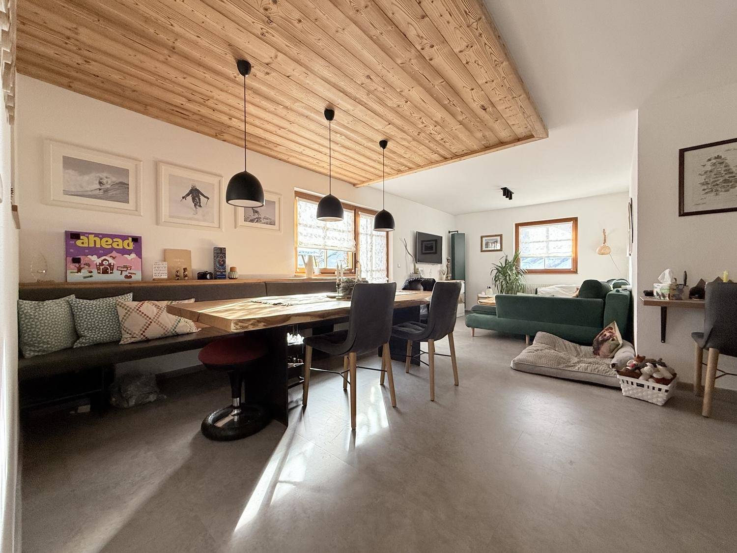 Großzügiger Wohn-Essbereich mit Holzbalkendecke, langem Esstisch und gemütlicher Sofaecke.