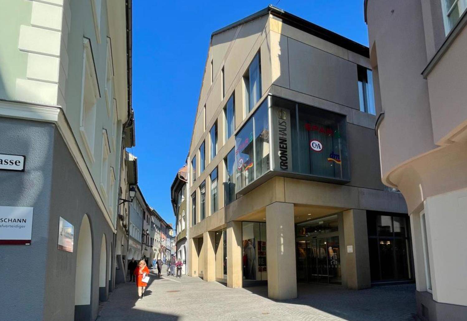 Gebäudeansicht in einer belebten Einkaufsstraße mit Geschäften und moderner Architektur unter blauem Himmel.