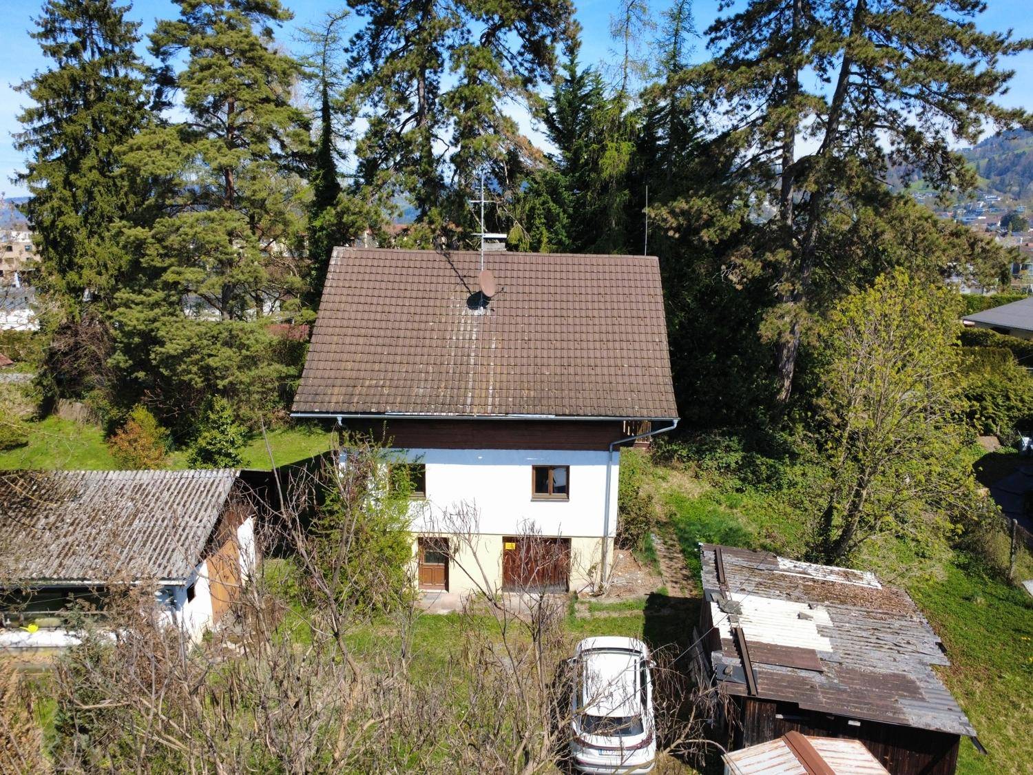 Frontansicht des Hauses mit Satteldach, umgeben von Bäumen und Grünflächen.
