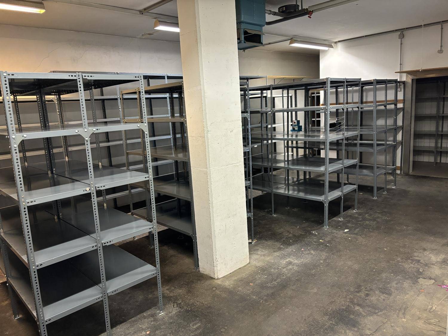 Großer Lagerraum im Untergeschoss mit zahlreichen Metallregalen und Betonboden.