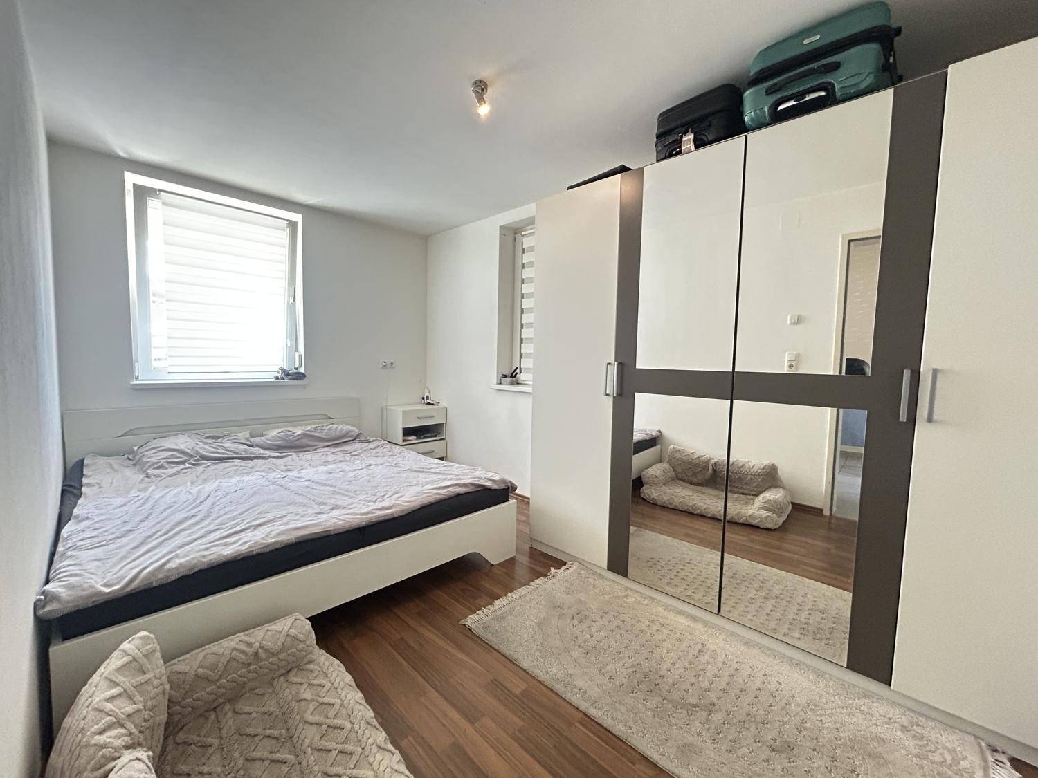 Geräumiges Schlafzimmer mit Doppelbett, Spiegelschrank und Laminatboden, hell durch zwei Fenster.