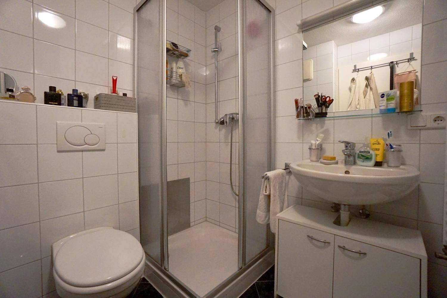 Badezimmer mit Duschkabine, WC und Waschbecken mit Unterschrank, komplett gefliest in Weiß.