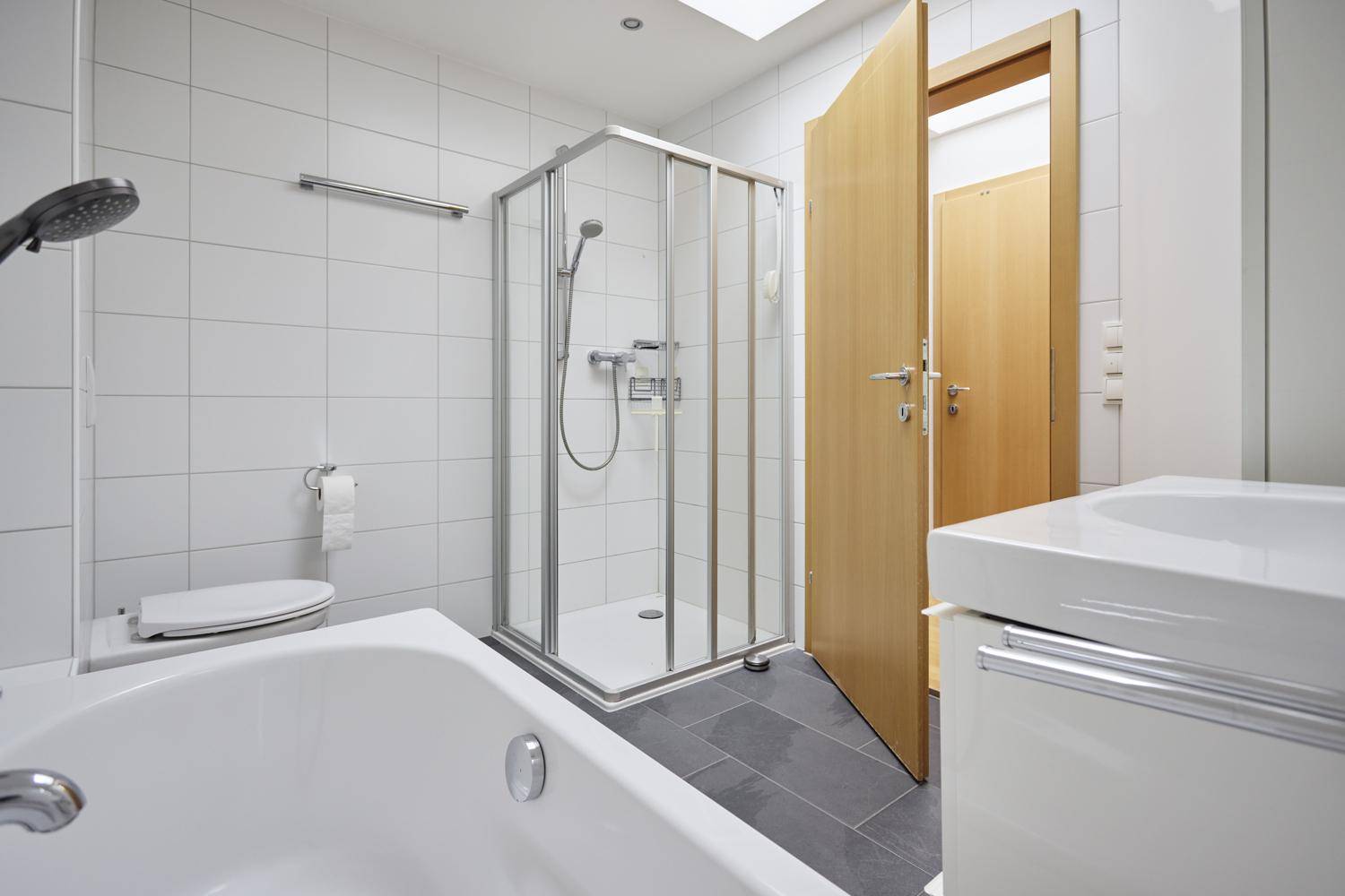 Helles Badezimmer mit Badewanne, Duschkabine und modernem Waschtisch.