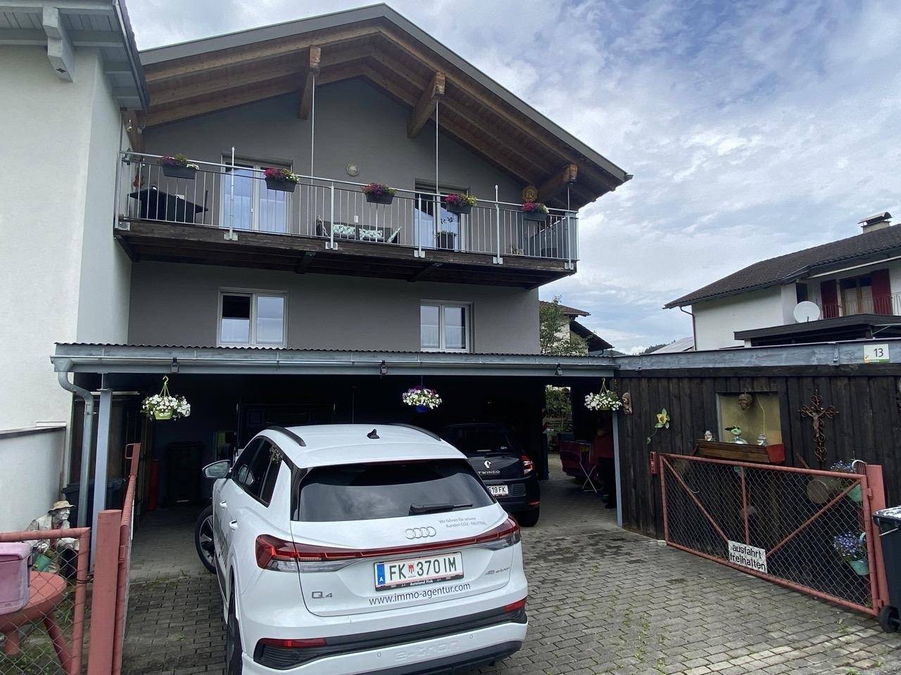 Ansicht des Hauses mit Carport und Balkon unter bewölktem Himmel.