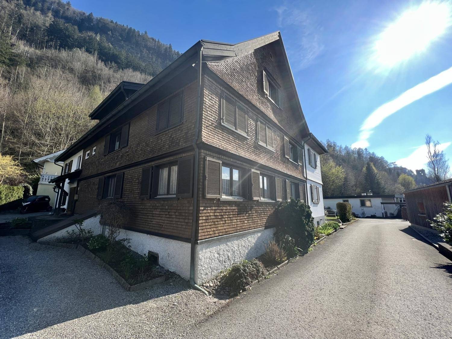 Traditionelles Gebäude mit Holzschindelfassade und Satteldach in bergiger Umgebung.