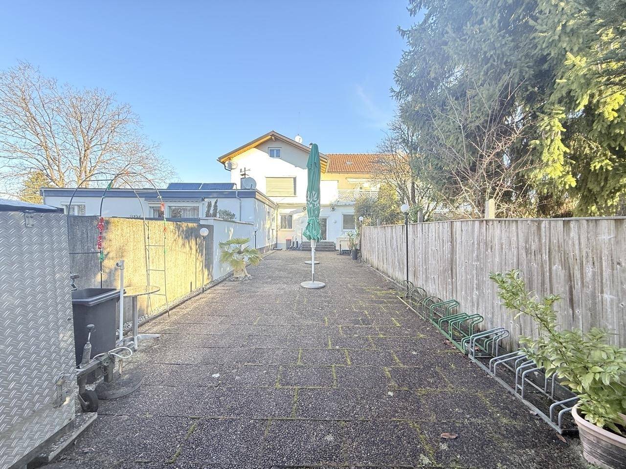 Hinterhof-Terrasse mit Sonnenschirmen, Holzzaun und Blick auf das Gebäude.