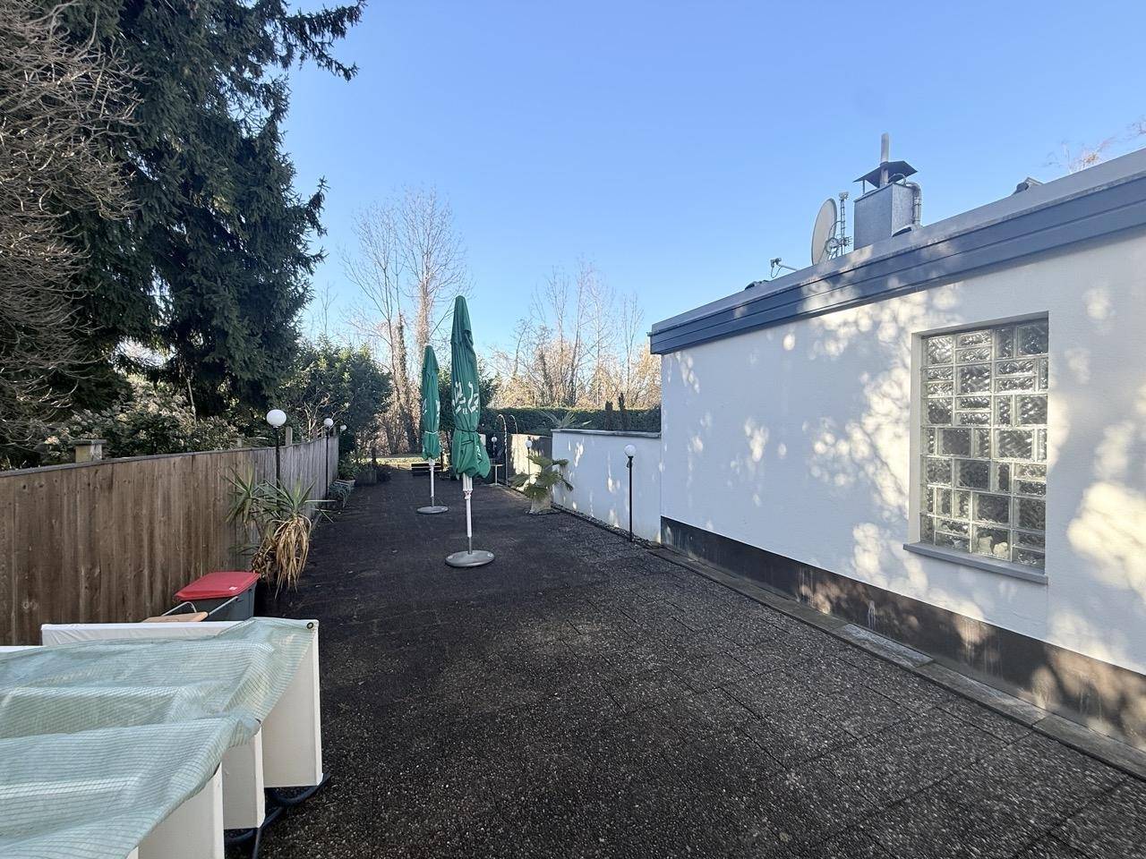 Lange gepflasterte Terrasse mit Sonnenschirmen und Blick auf die Rückseite des Gebäudes.