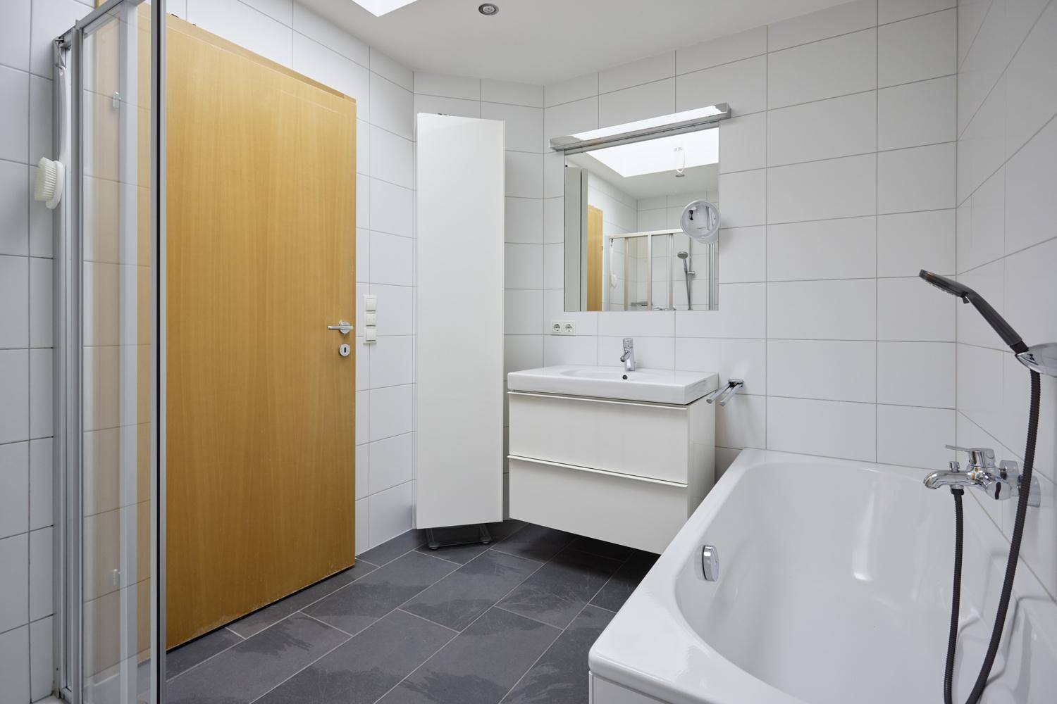 Modernes Badezimmer mit Badewanne, Dusche und grauen Bodenfliesen.