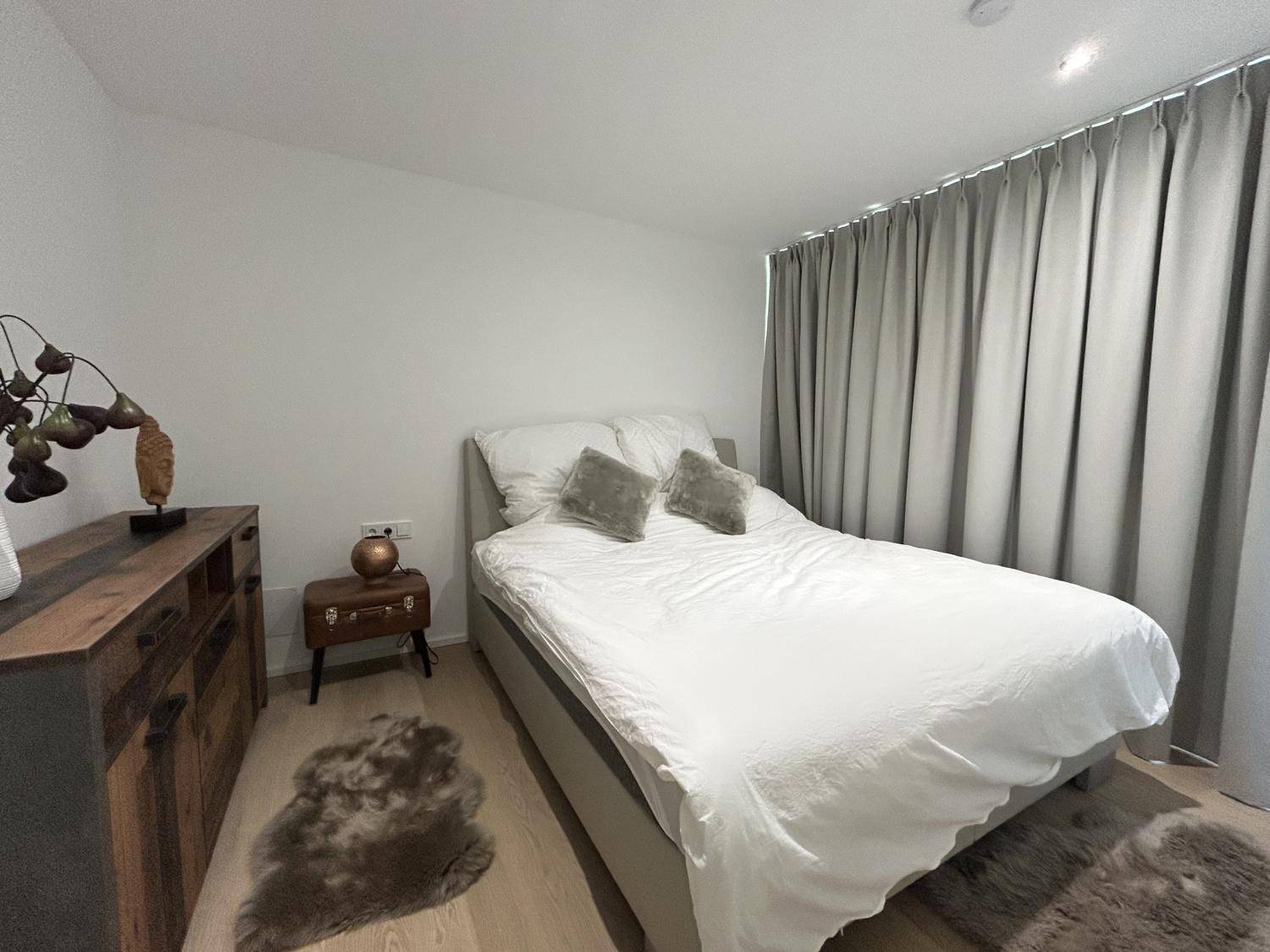 Gemütliches Schlafzimmer mit Holzboden, großem Bett und dunklen Vorhängen für Privatsphäre.