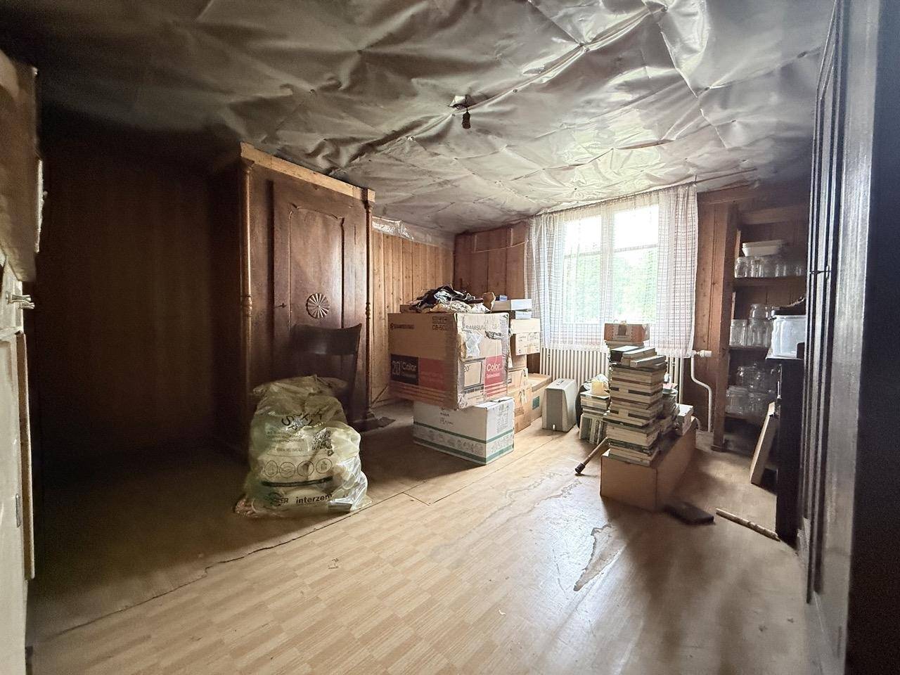 Abstellraum im Kellergeschoss mit Holzverkleidung, Fenster und gelagerten Gegenständen.