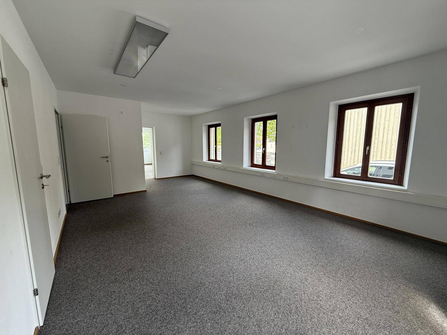 Heller Büroraum mit Teppichboden und braunen Fensterrahmen, ideal für Arbeitsbereiche.
