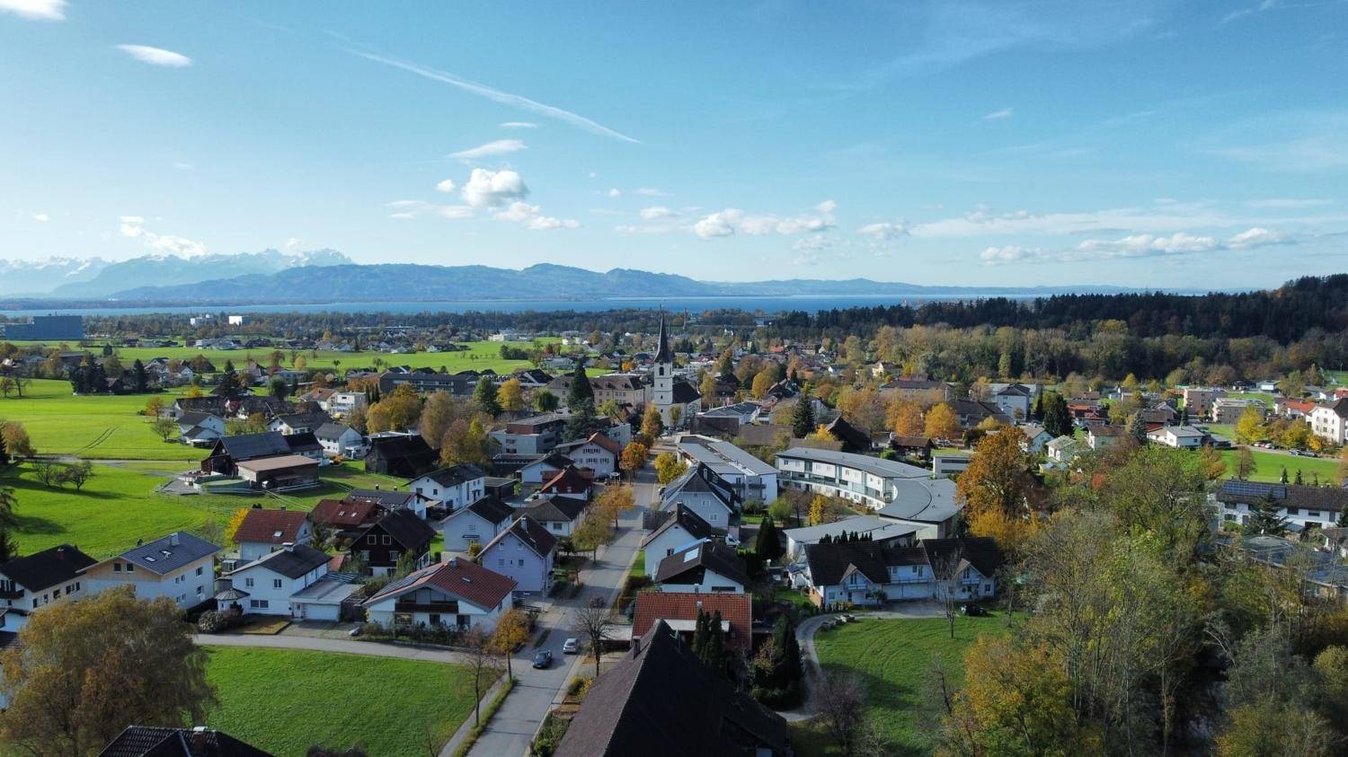 Panoramablick auf ein idyllisches Dorf mit See und majestätischen Bergen am Horizont.