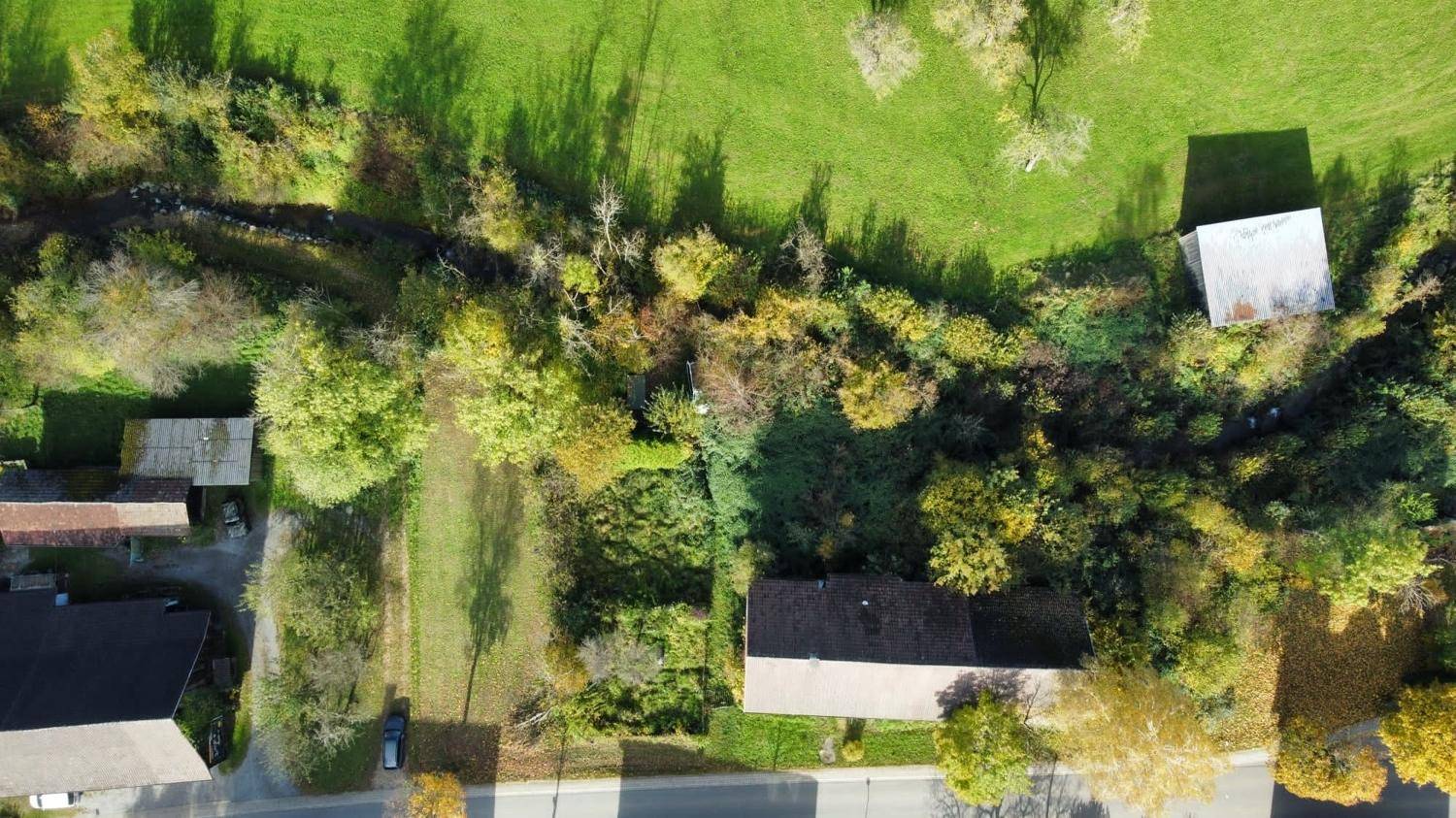 Luftbild eines Grundstücks mit Haus, Straße, grünen Flächen und einem Bachlauf.