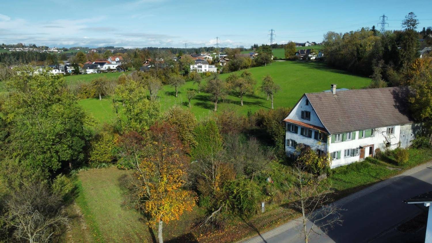 Luftaufnahme eines Hauses mit braunem Dach, umgeben von grünen Wiesen und Bäumen.