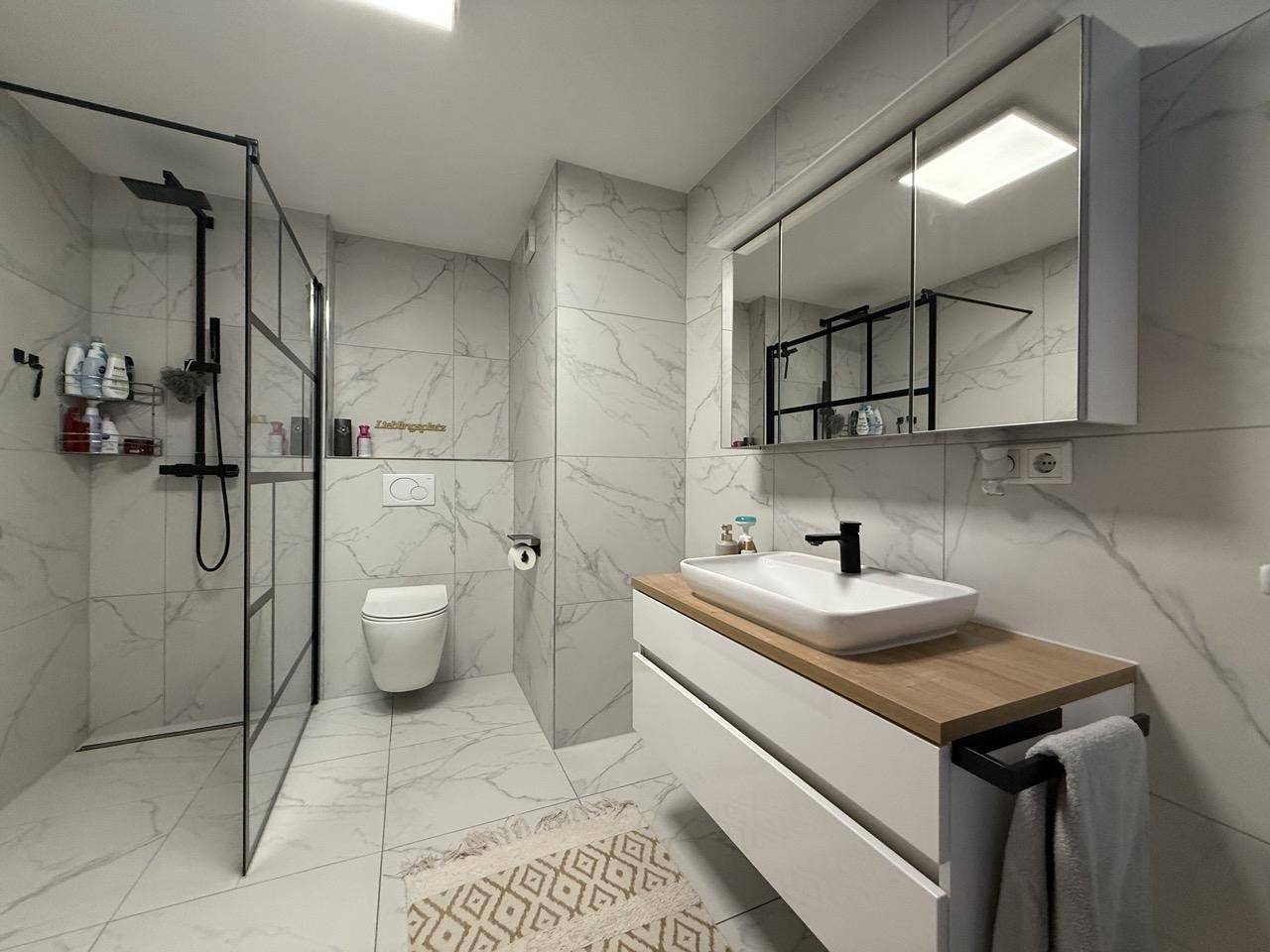 Modernes Badezimmer mit begehbarer Dusche, Wand-WC und eleganten Marmorfliesen.