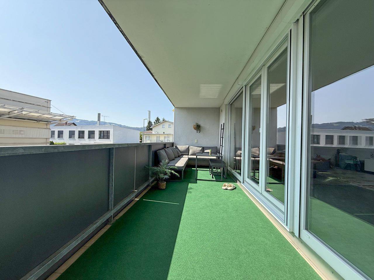Geräumiger Balkon mit Kunstrasen, Sitzgelegenheiten und Blick auf die Umgebung.