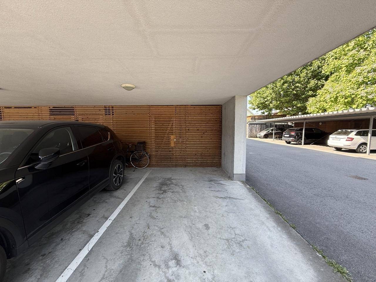 Überdachter Parkplatz mit Betonboden und Holzverkleidung.