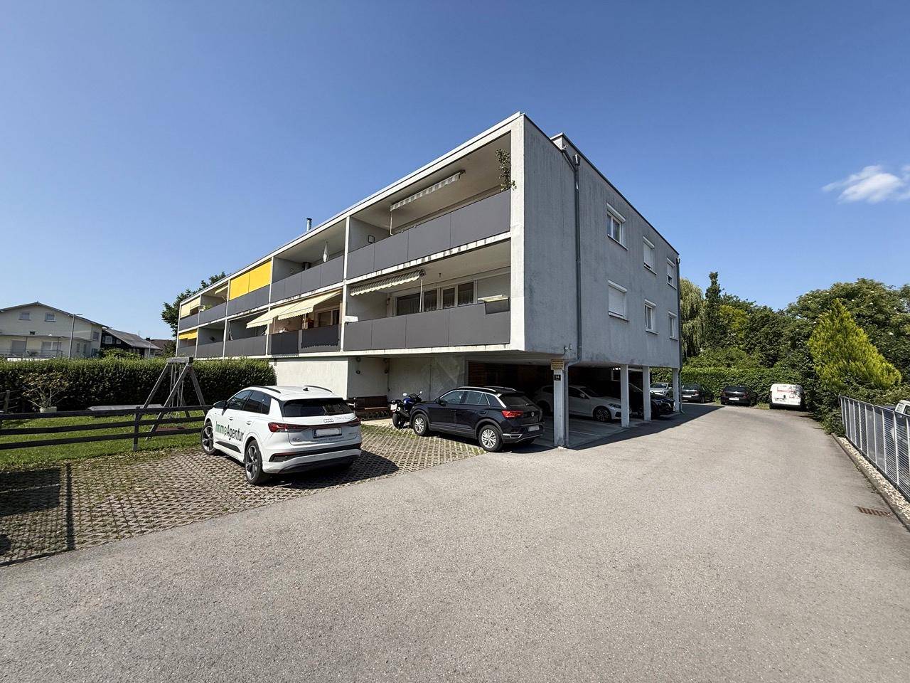 Mehrfamilienhaus mit Balkonen und überdachten Parkplätzen im Freien.