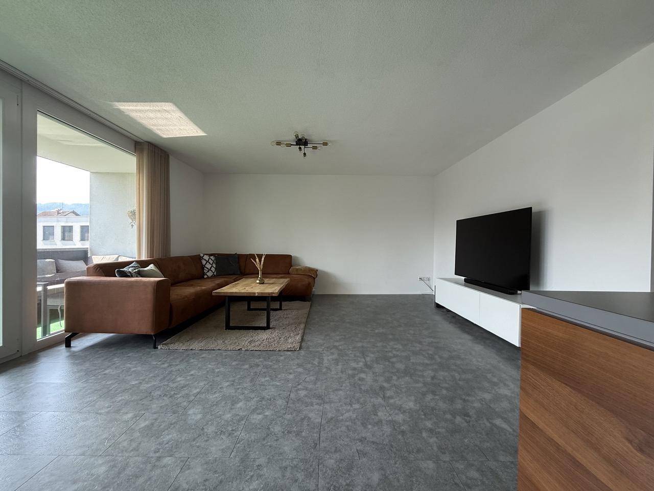 Helles Wohnzimmer mit bequemer Couch, Fernseher und Zugang zum Außenbereich.