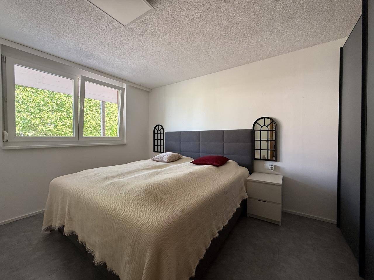 Schlafzimmer mit Doppelbett, Nachttischen und Blick ins Grüne durch das Fenster.