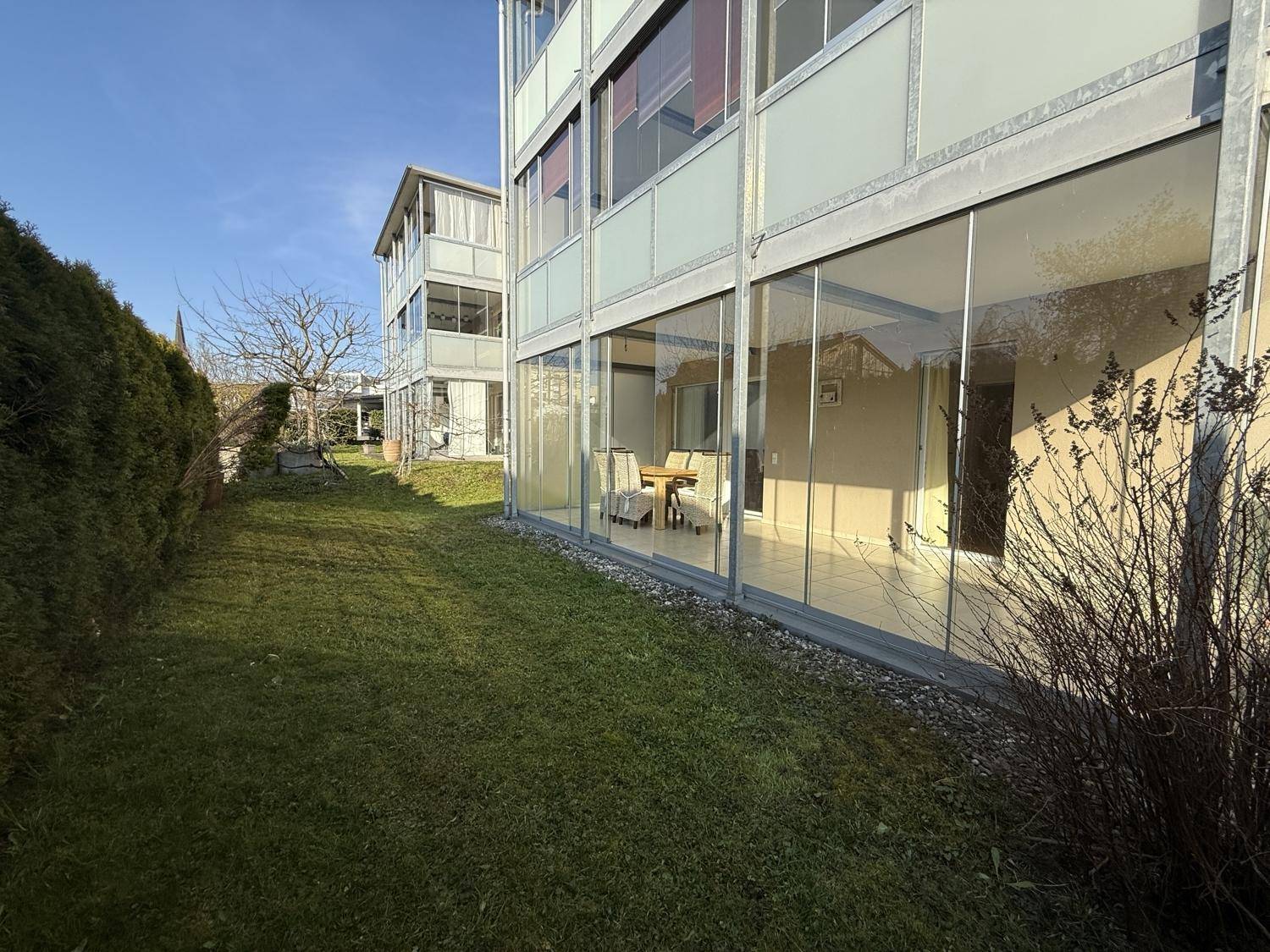 Außenansicht des Gebäudes mit gepflegtem Rasen und einer verglasten Terrasse im Erdgeschoss.