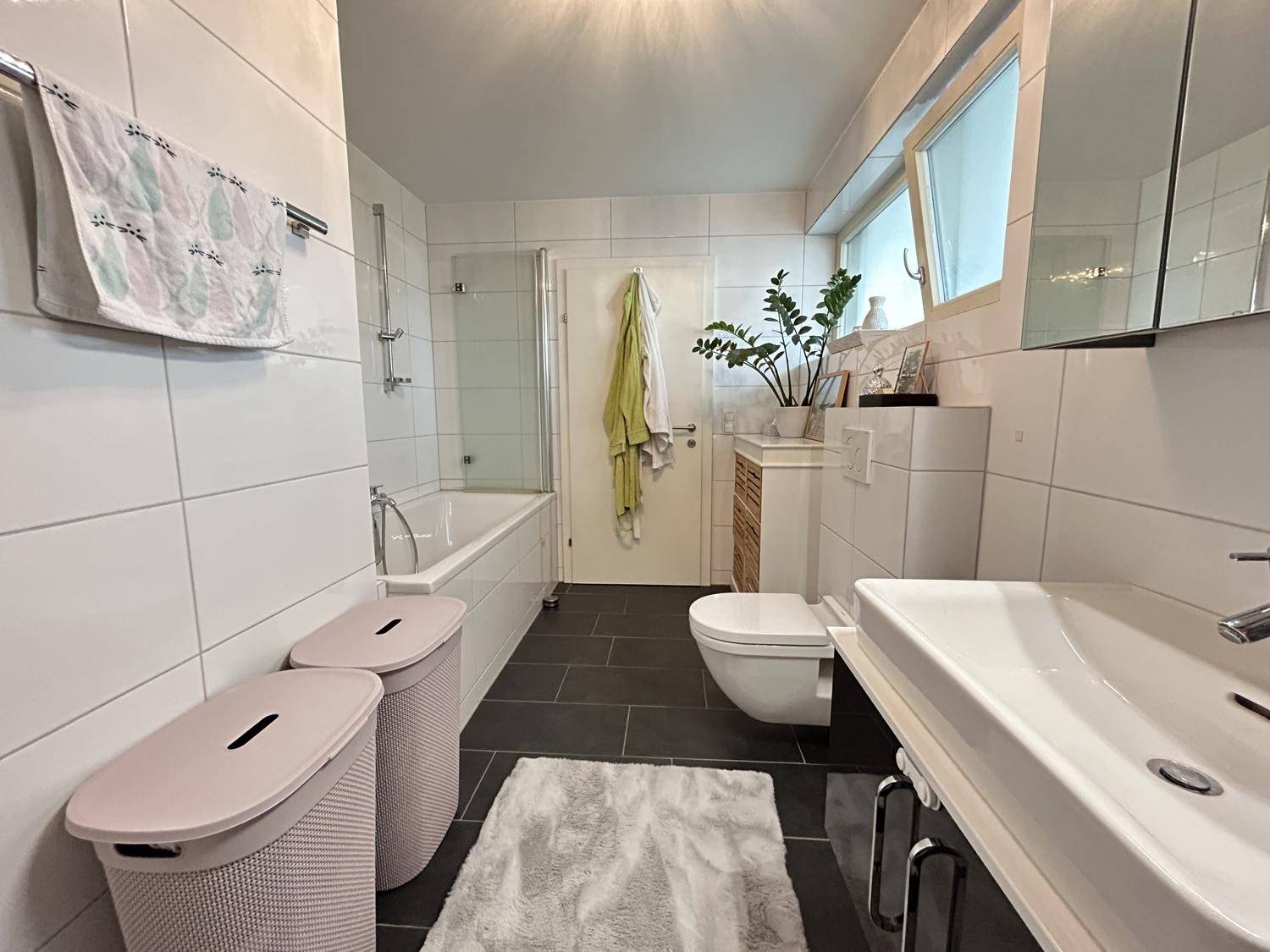 Modernes Badezimmer mit Badewanne, WC, Einzelwaschbecken und Fenster.