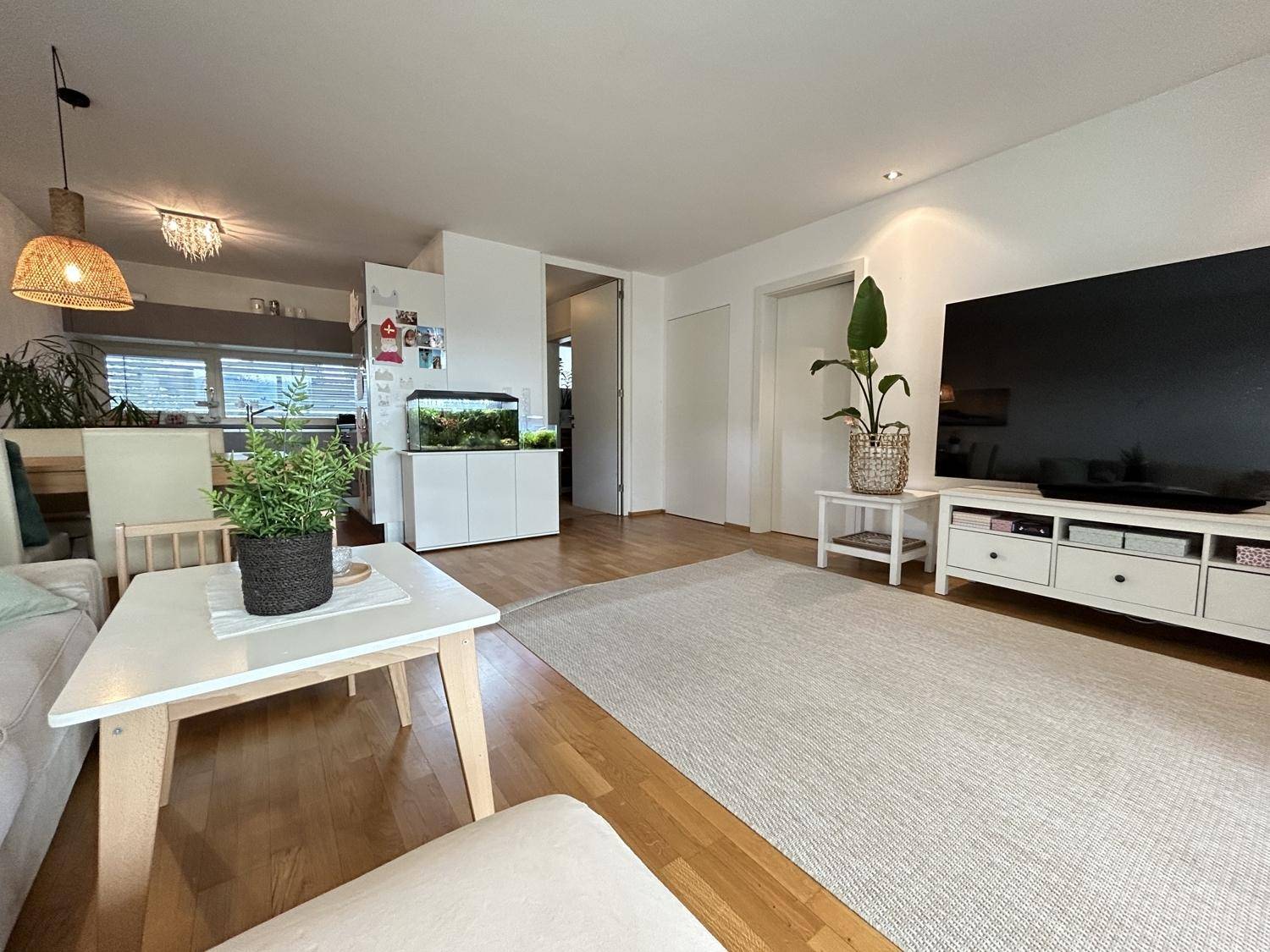 Geräumiges Wohnzimmer mit hellem Teppich, Fernseher und Übergang zum Essbereich.