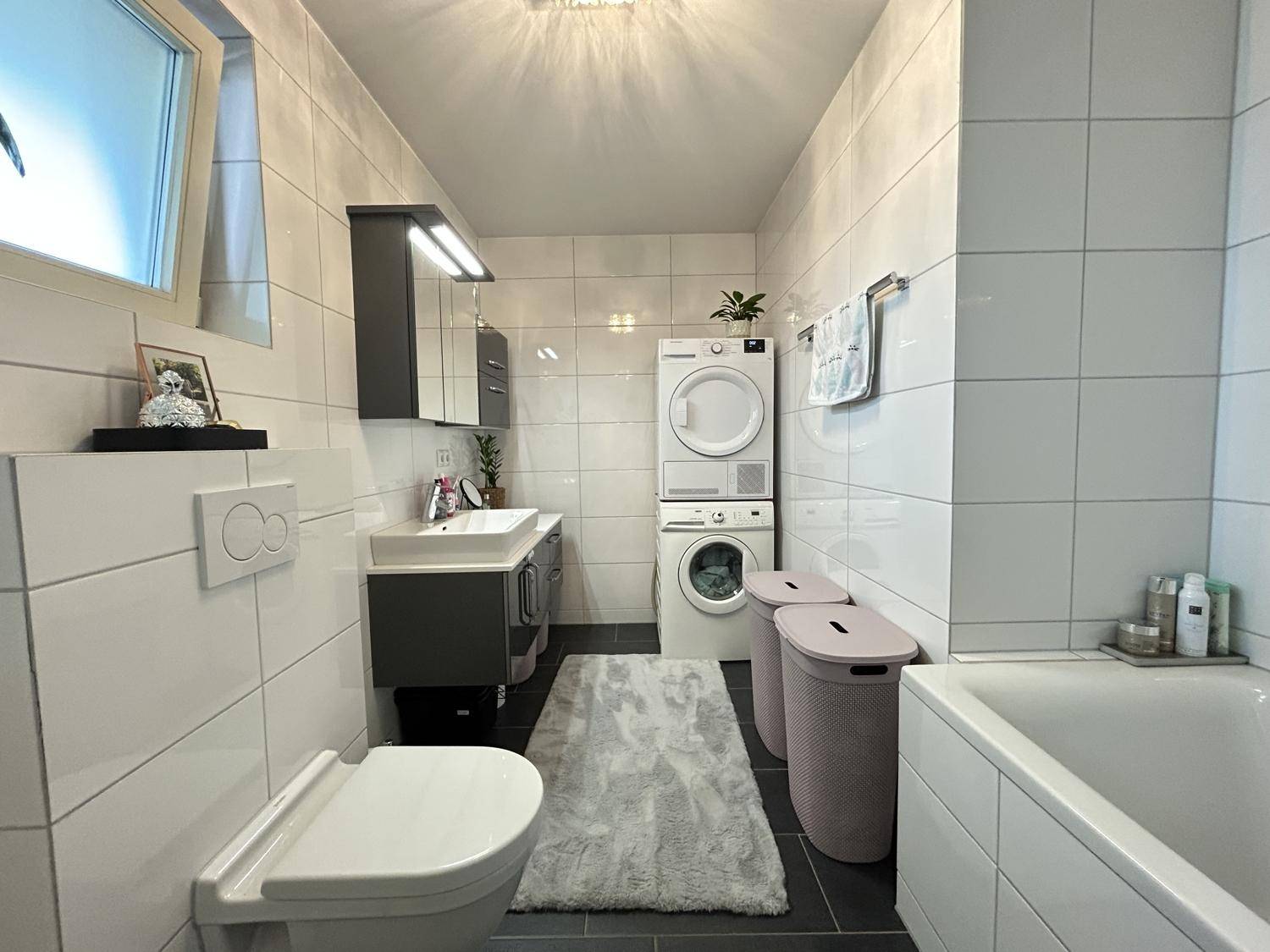 Helles Badezimmer mit Badewanne, Waschmaschine, Trockner und modernem Waschtisch.