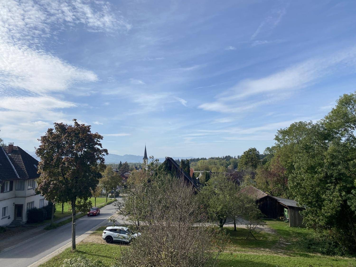 Aussicht auf eine grüne Landschaft mit Straße, Häusern und einem Kirchturm im Hintergrund.