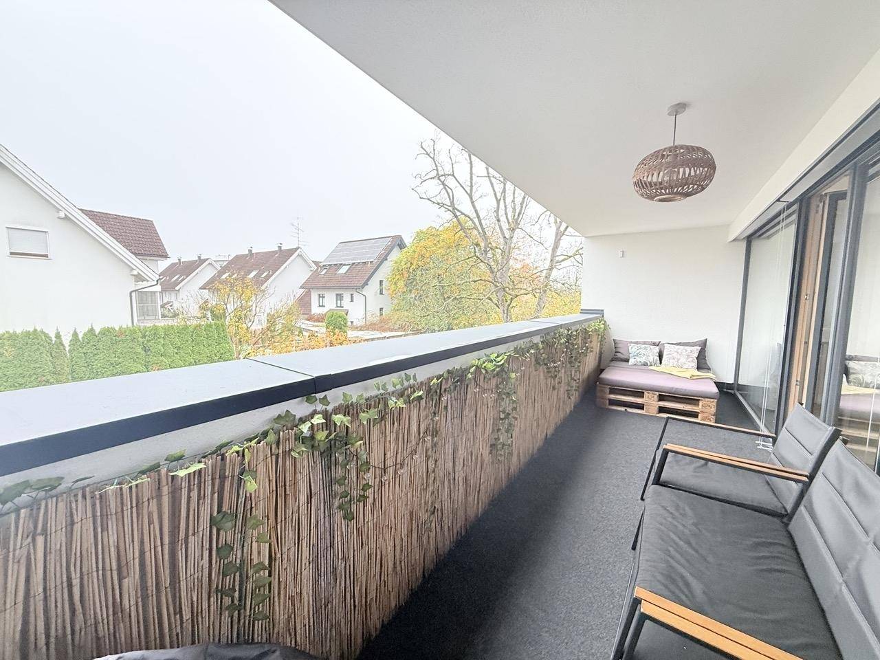 Heller Balkon mit Sitzgelegenheiten, Sichtschutz und Blick auf die umliegenden Häuser.