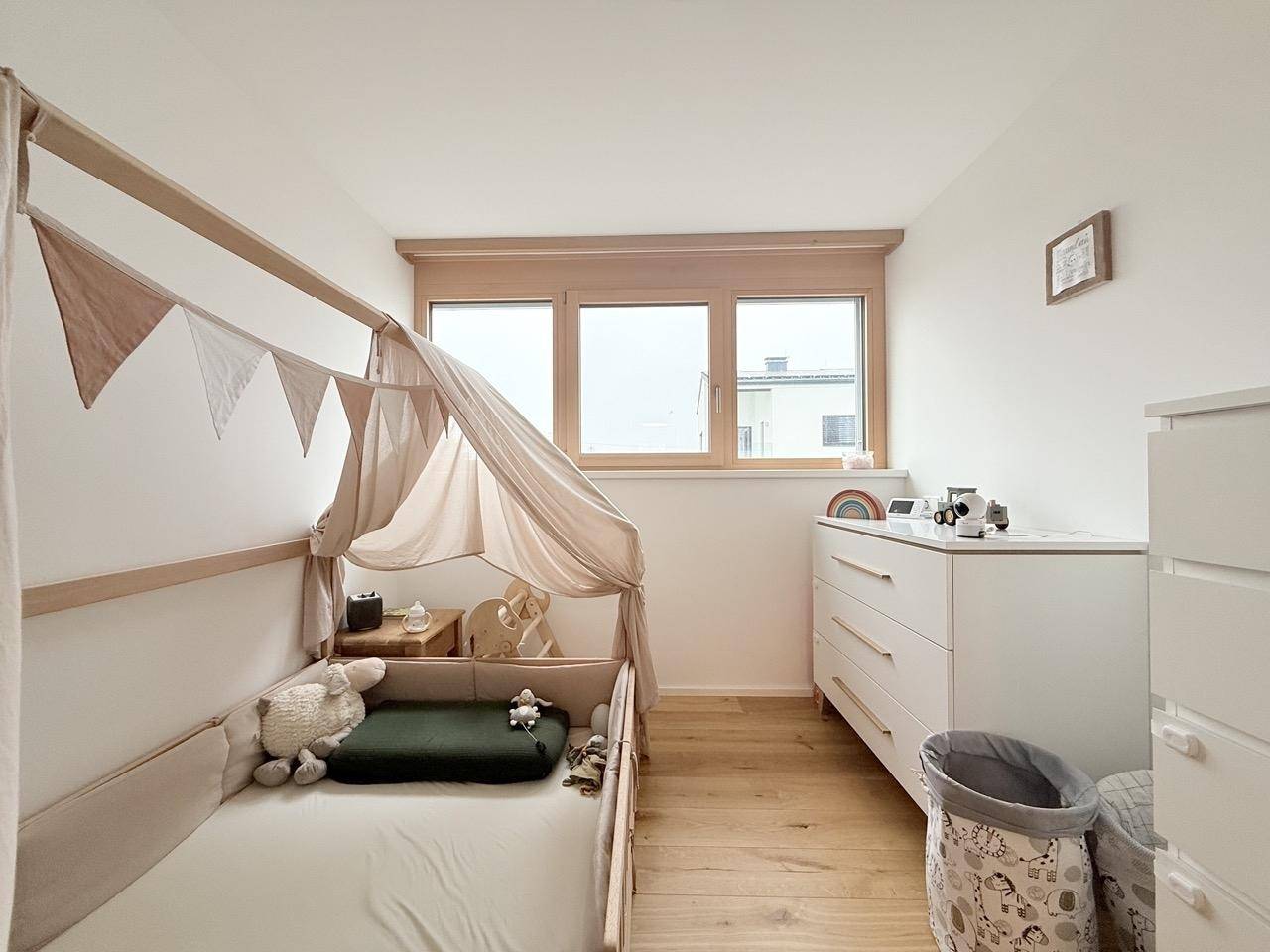 Kinderzimmer mit Holzboden, hellem Bett und Fenster für viel Tageslicht.