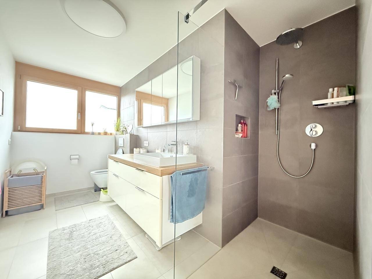 Modernes Badezimmer mit begehbarer Dusche, großformatigen Fliesen und Fenster für Tageslicht.