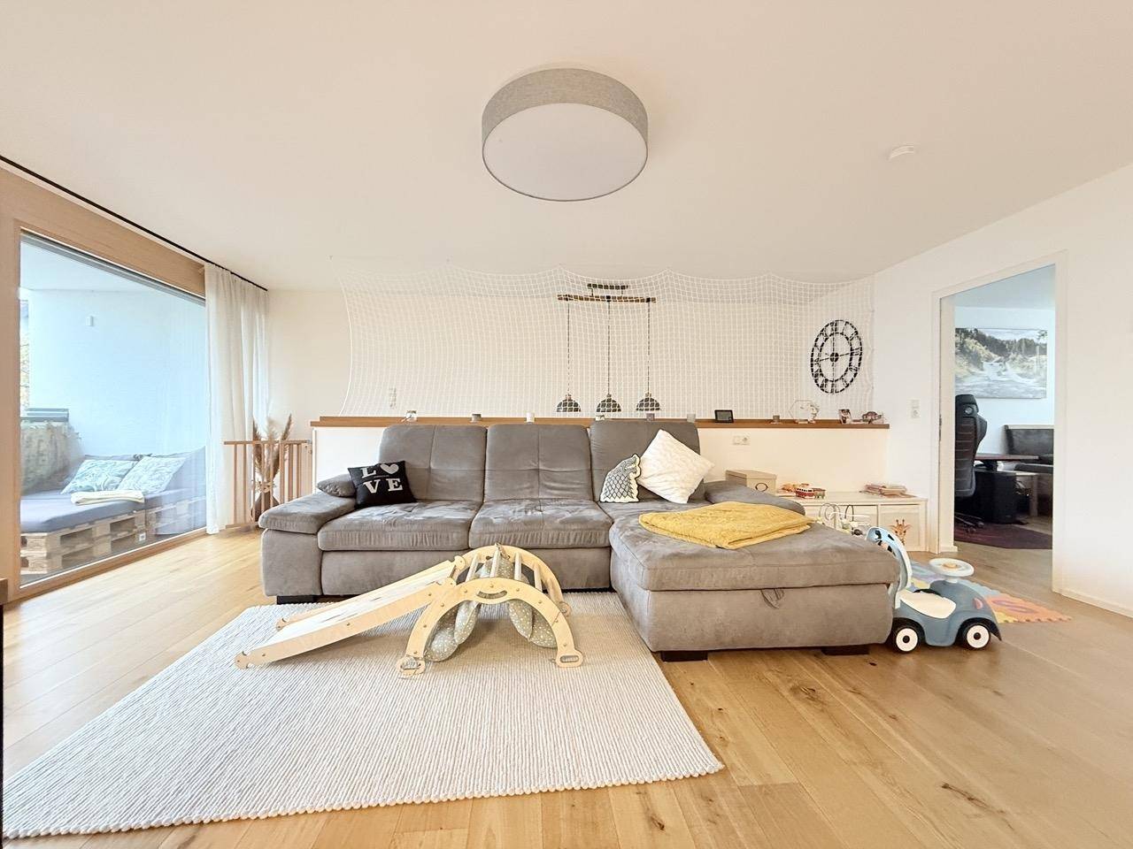 Gemütliches Wohnzimmer mit großem Ecksofa, Holzboden und Zugang zu einem Balkon.