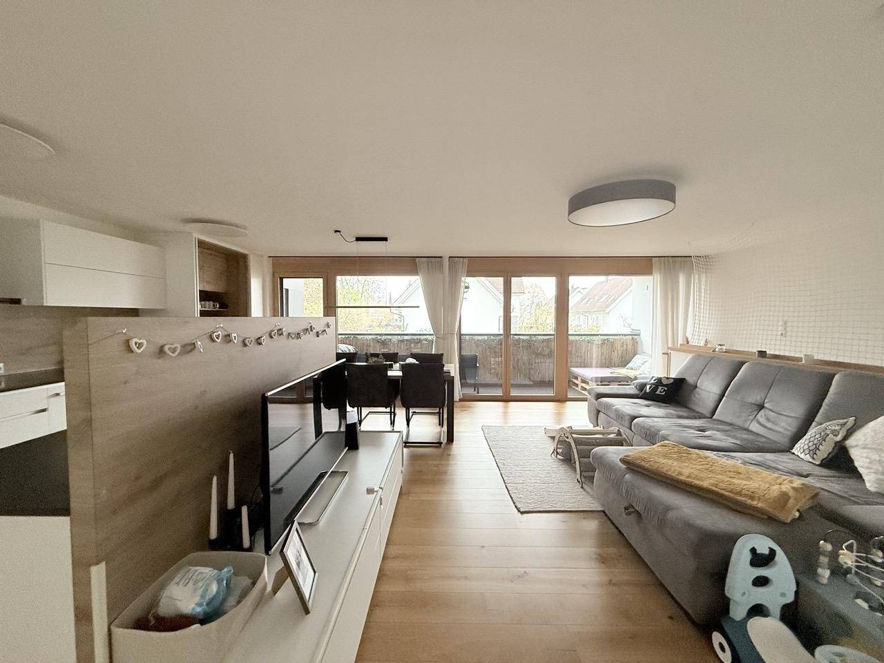 Geräumiger Wohn- und Essbereich mit Sofa, TV-Möbel und Zugang zum Balkon.