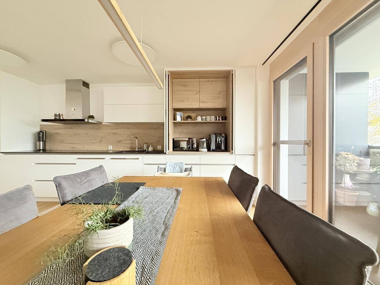 Moderne Einbauküche mit Holzakzenten, Esstisch und Zugang zum Balkon.