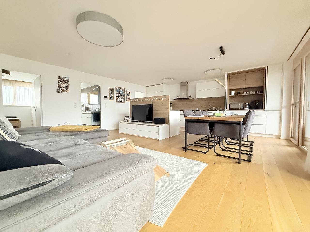Geräumiger Wohn- und Essbereich mit Holzboden, Sofa und integrierter Küche in hellem Design.