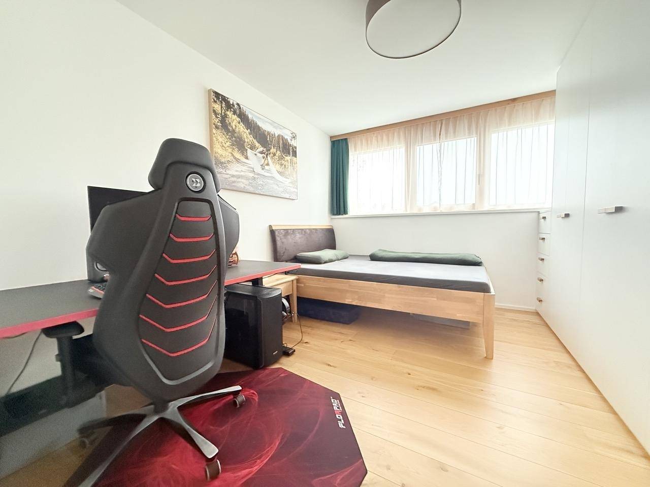 Schlafzimmer mit Holzboden, Einzelbett, Schreibtisch und großem Fenster für viel Licht.