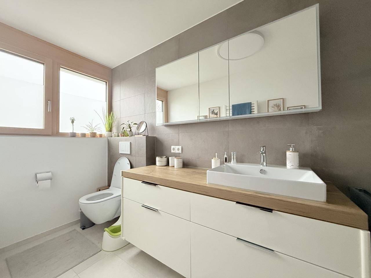 Helles Badezimmer mit modernem Waschtisch, Toilette und Fenster für natürliche Belüftung.