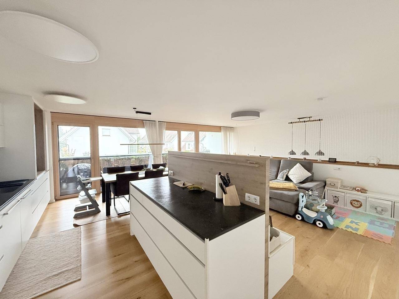 Offener Wohn- und Essbereich mit moderner Küche, Holzboden und Zugang zum Balkon.