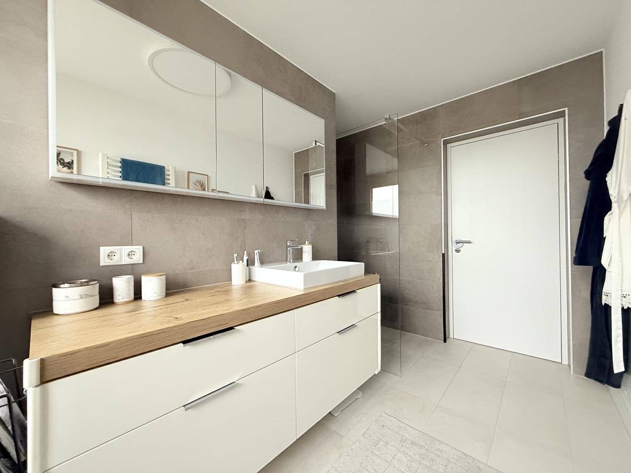 Elegantes Badezimmer mit modernem Waschtisch, großem Spiegelschrank und grauen Fliesen.