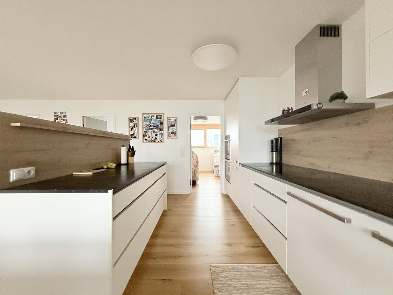 Moderne Küche mit Kochinsel, weißen Fronten und Holzboden in offenem Wohnkonzept.