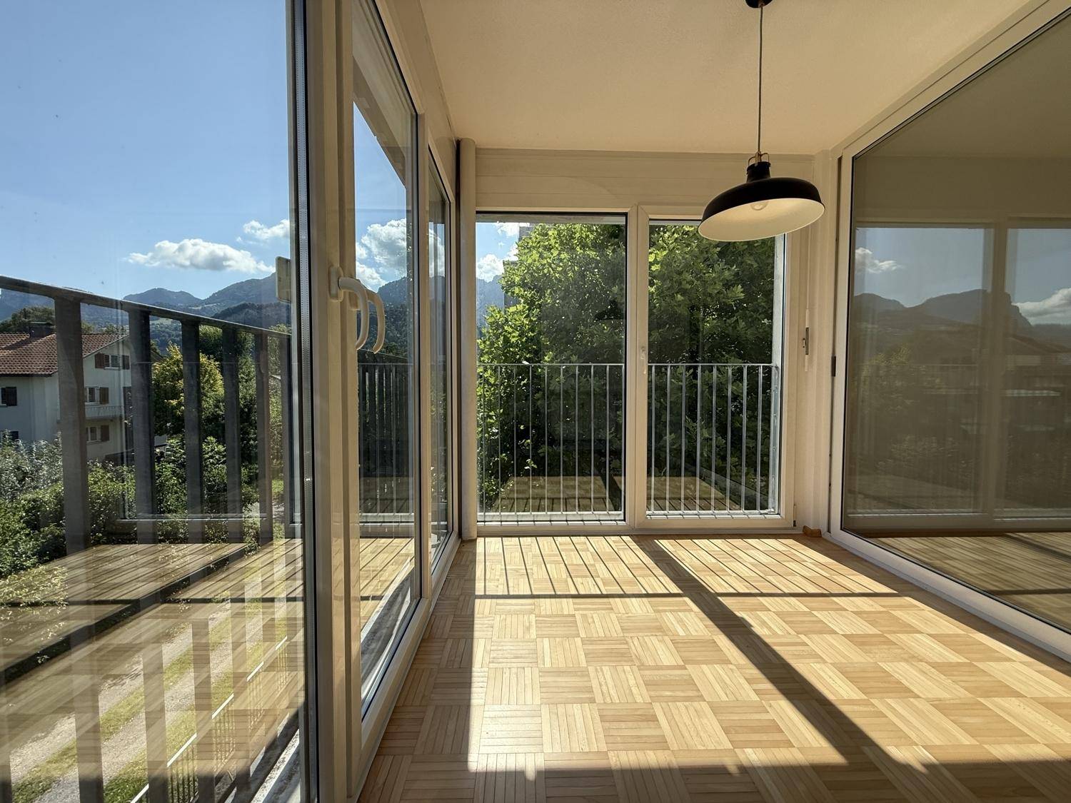 Verglaste Loggia mit Parkettboden, Bergblick und viel Tageslicht durch große Fenster.