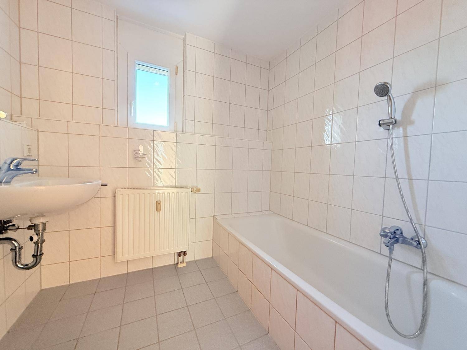 Gefliestes Badezimmer mit Badewanne, Dusche, Einzelwaschbecken und Fenster für Tageslicht.